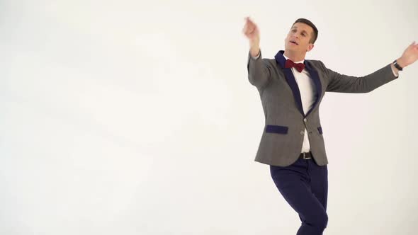 humorist in gray suit with red bow tie is dancing in the similitude of dancer with ribbon in hand alt