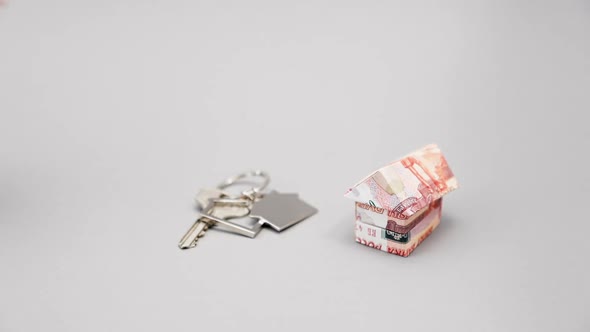 Close up of key with keychain and origami from russian rubles. Female hand take out a paper house alt