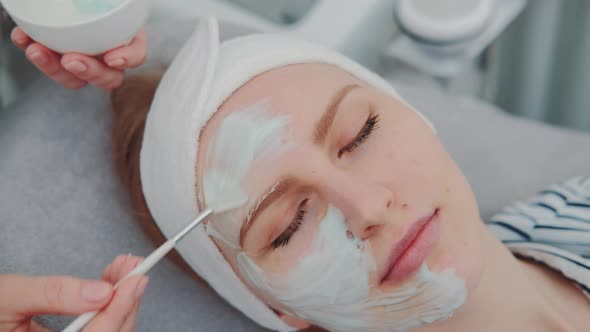 Close-up Shot of Cosmetician Hands Applying Cream Mask on Young Woman's Face at Beauty Spa Salon