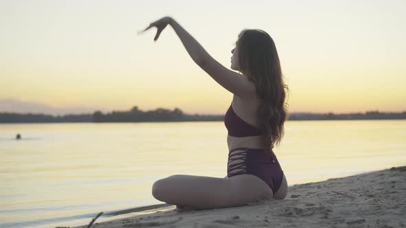 Angle View of Relaxed Slim Woman Sitting in Lotus Pose on Sandy Beach at Sunset. Portrait of alt