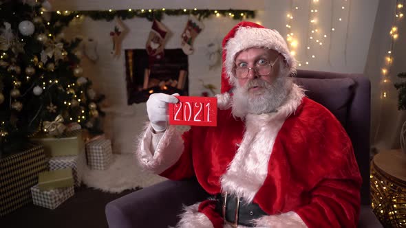 Portrait of Funny Santa Claus in Glasses, Sitting in His Rocking Chair Near the Christmas Tree