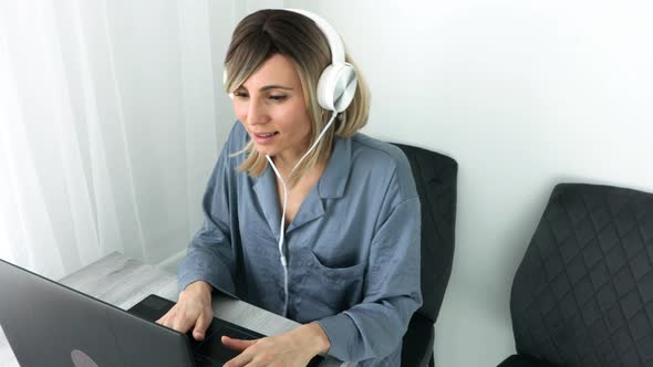 Attractive european blonde woman in headphones listening music and dancing sitting on comfy chair