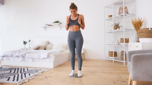 Sporty Woman in Sportswear Standing on Scales Crossing Fingers Unhappy About Weight Loss alt