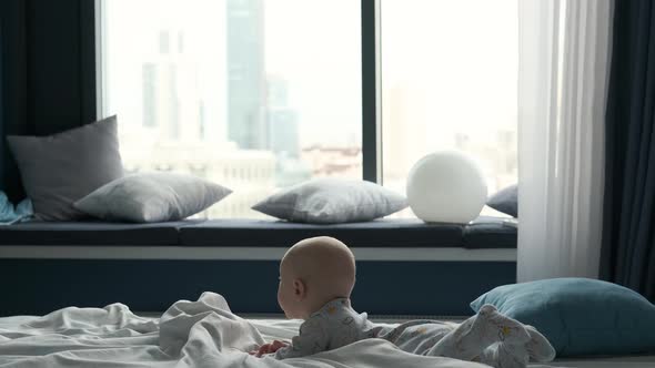 portrait of a toddler lying in bed against the background of a large window