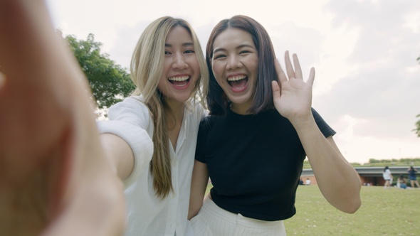 Two young female friends take selfies and video calls on smartphones.