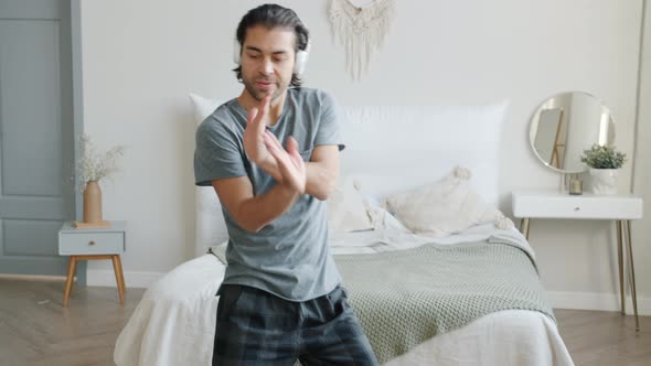 Slow Motion of Good-looking Man Wearing Pajamas Dancing in Bedroom Wearing Headphones alt