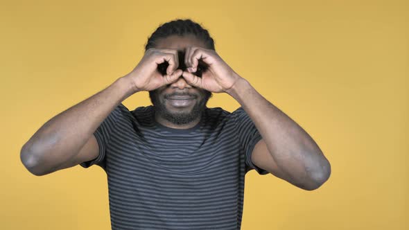Casual African Man Searching with Handmade Binoculars Isolated on Yellow Background alt