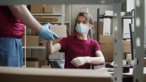Man Employee of Warehouse Wearing Medical Mask and Protective Gloves Receiving Delivery Box and alt