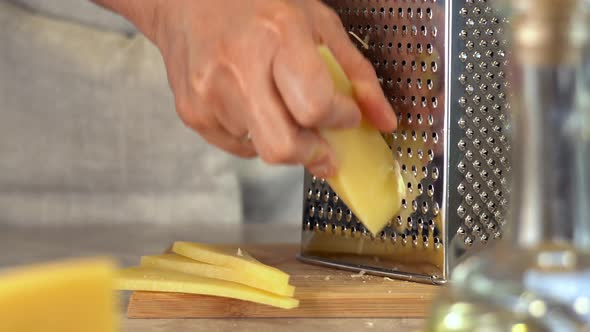 Male Hands Grate on Grater Yellow Parmesan Cheese on Wooden Cutting Board