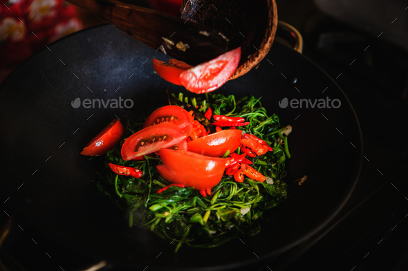 Adding red sliced tomato into water spinach stir-fry, close up