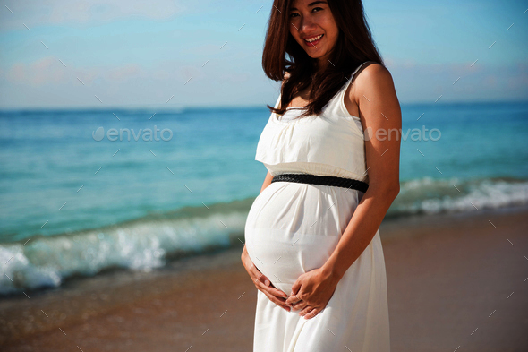 Asian pregnat woman smile into camera while touching her belly