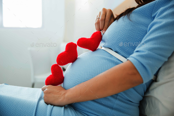Asian young pregnant woman put heart shape accessories in her tu