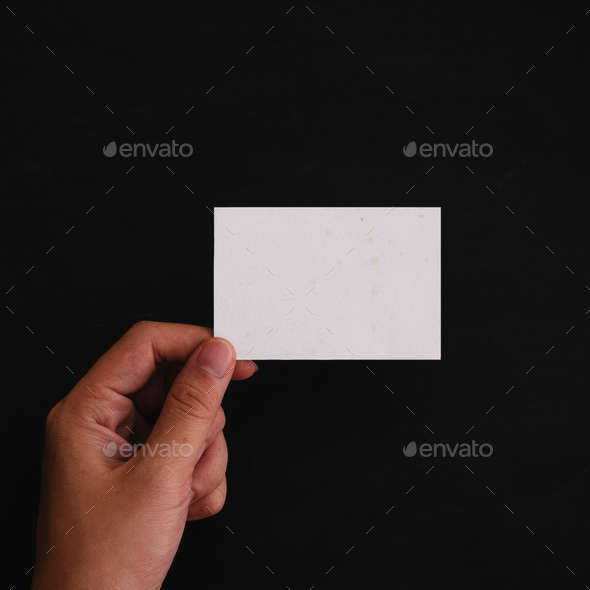 Hand holding a blank white card. black background. Mock Up