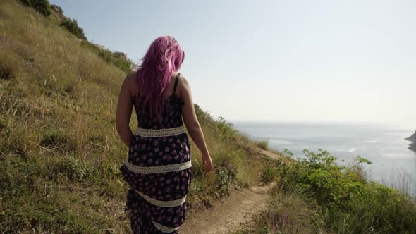 Woman with Pink Hair Walks Along a Narrow Path To the Sea