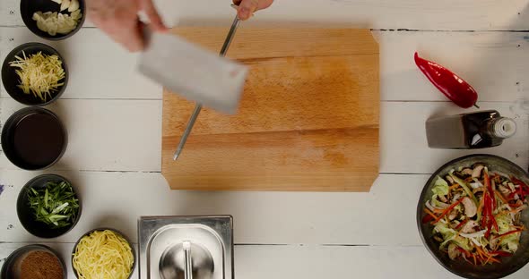 Chef's Hands Sharpen a Large Knife at the White Table on Working Ingredients alt