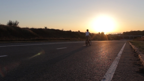 Young Boy On His Bike On The Road In Sunset