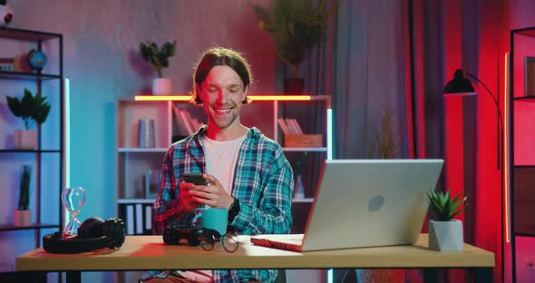 Guy Which Sitting at the Table at Home in the Evening and Watching Comedy on Laptop alt