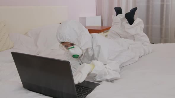 A Boy in a Protective Suit and a Respirator at Home at a Computer Isolated During an Epidemic alt