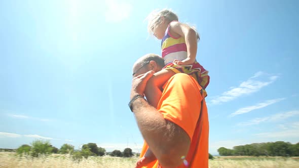 Grandfather Carrying Grand Daughter On Shoulders In Nature In Summer alt