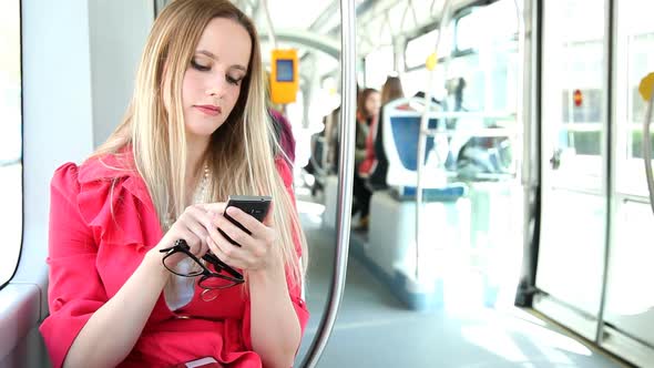 Young Blond Woman Riding Tram Typing On Mobile Phone Cell Holding Glasses 3 Stock Footage 2272