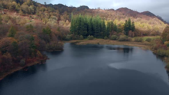 Aerial footage of Yew Tree Tarn in Cumbria in Autumn with the trees in colour. alt