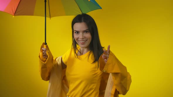 Happy Charming Woman in a Yellow Raincoat is Standing Under the Rainbow Umbrella alt