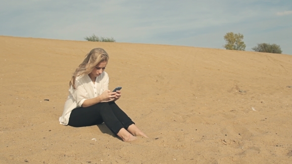 Barefoot Girl Sitting On The Sand With The Phone