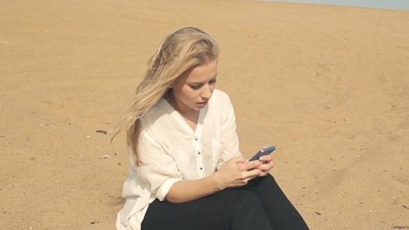 Beautiful Girl Sitting On The Sand With The Phone