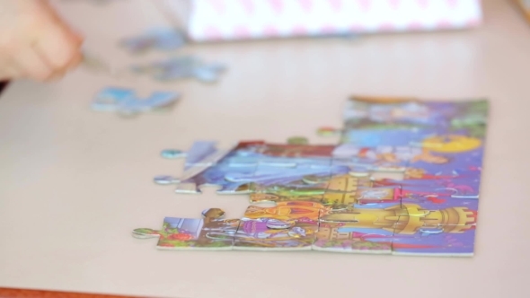 Hands Of Little Child Doing A Puzzle At Table