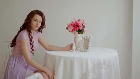 Beautiful Brunette In a Pink Dress Sits At a Table