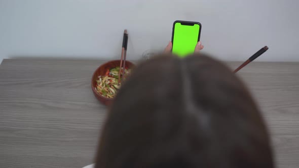 Woman Using Smartphone With Green Screen While Sitting With Food On The Table alt
