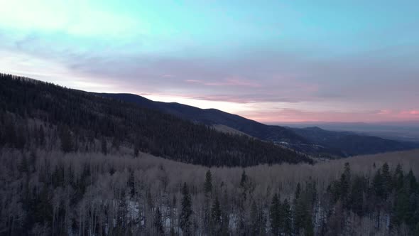 A drone shot over top of a mountain peak with forest and sunrise alt