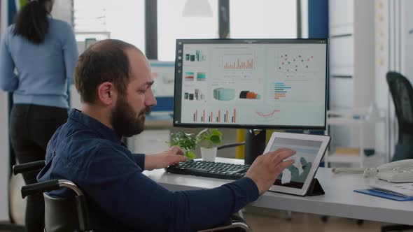 Handicapped Man Employee Sitting in Wheelchair Working at Notepad and Computer alt