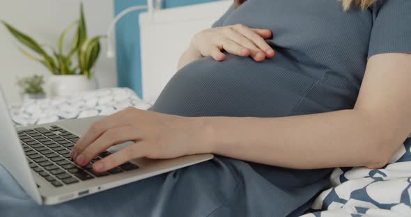 Young Pregnant Woman Work on a Laptop Lying Down on Bed in Domestic Environment