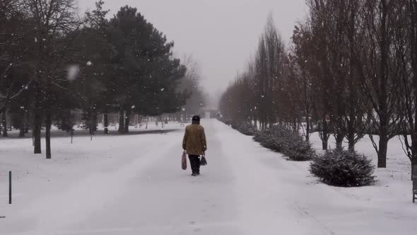An Old Man Veteran Walking in the Snowy Park While Snowfall