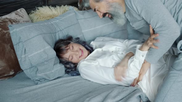 Joyful Husband Tickling Cute Young Wife Having Fun with Woman Then Kissing in Bed at Home alt