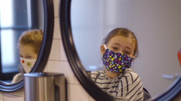 Reflection in Mirror of Preteen Schoolgirls Wearing Colorful Safety Mask and Washing Hands in Public alt
