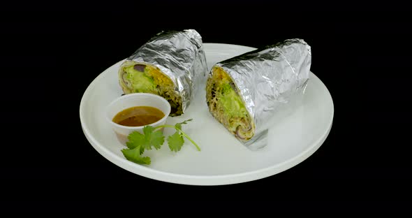 Foil-wrapped burrito on a turntable with mild sauce. Mexican food. alt