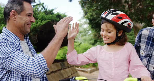 Girl sitting on a bike while happy parents giving high five and hugging her alt