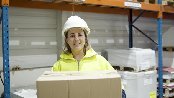 Happy Female Employee Holding Cardboard Box in Warehouse alt