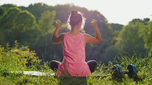 The Teen Girl Is Exercising with Dumbbells Outdoors alt