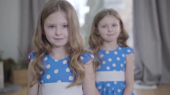 Camera Approaching To Two Beautiful Little Caucasian Girls Posing Indoors. Brunette Twin Sisters alt