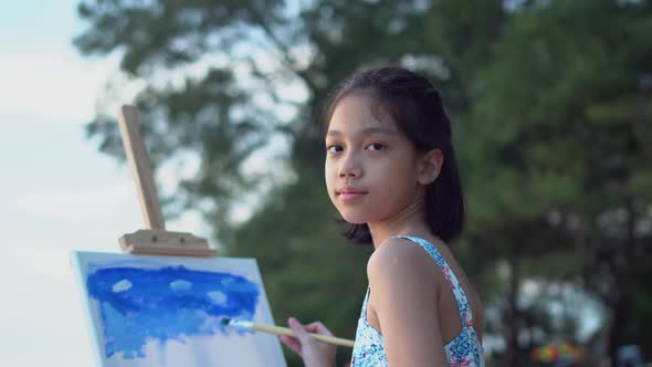 Asian kid painting on the canvas at the beach. Happy child girl drawing a picture outdoors