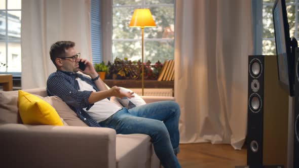 Side View of Young Man Talking on Smartphone and Watching Tv at Modern Apartment alt