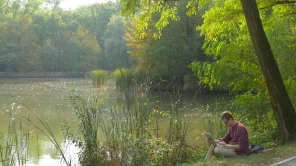 Man in Glasses is Sitting at the Lake Bank alt