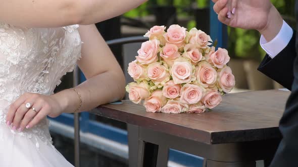 The Bride and Groom on Their Wedding Day Sitting at a Table with the Bridal Bouquet alt