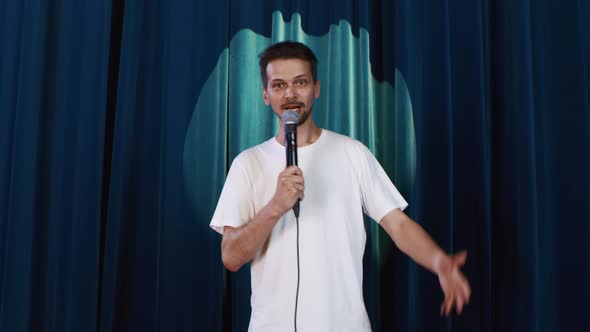 Comic Man Presents Standup Performance on Stage with Microphone Against Curtain