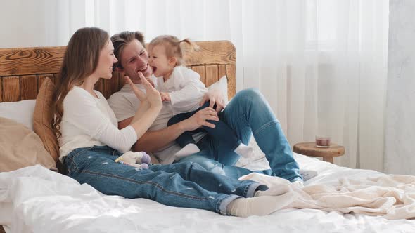 Young Caucasian Parents with Little Daughter Kid Toddler Infant Lying in Cozy Bed Mom Playing Patty alt