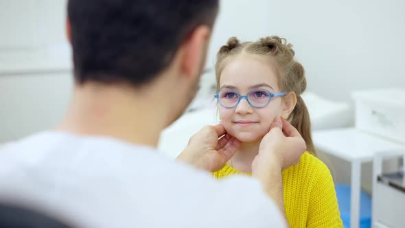 Shooting Over Doctor Shoulder of Cute Smiling Girl Looking at Pediatrician Checking Thyroid alt