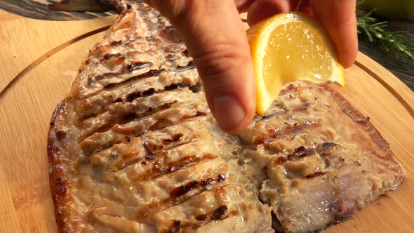 Hand is Squeezing Slowly Lemon Juice on the Grilled White Mackerel Fish Fillet alt